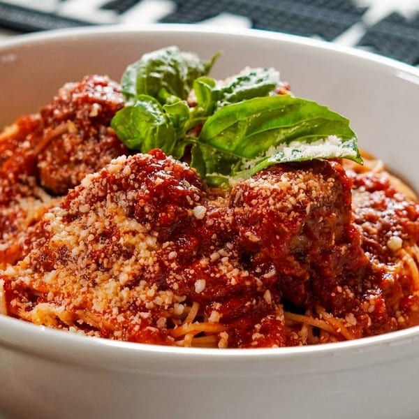 Spaghetti and meatballs with marinara sauce, parmesan cheese, and fresh basil in a white bowl.