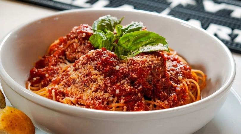 Spaghetti and meatballs with marinara sauce, parmesan cheese, and fresh basil in a white bowl.