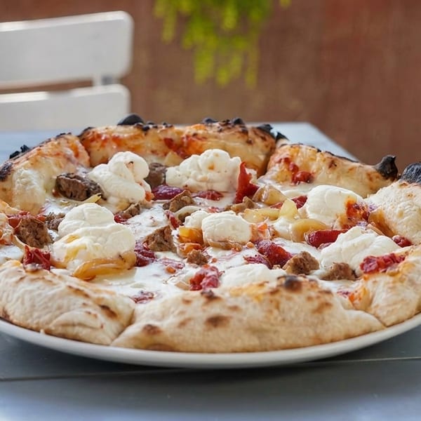 A white pizza with dollops of ricotta, sausage, and red peppers on a white plate.