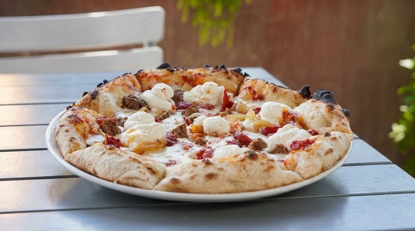 A white pizza with dollops of ricotta, sausage, and red peppers on a white plate.